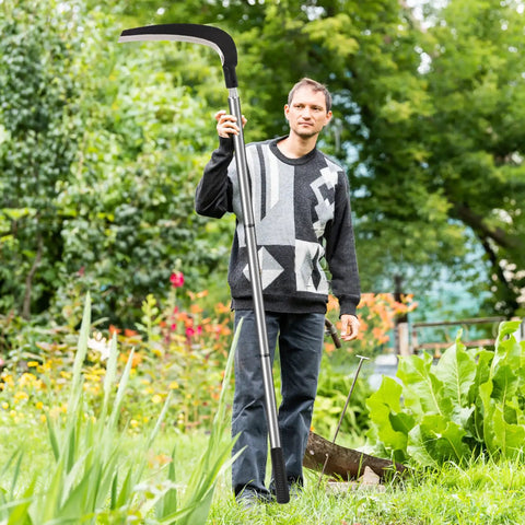 Person holding Beast Scythe Tool For Grass Cutting And Weeding Sickle Garden Tool with adjustable long handle in a garden.