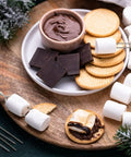 Ingredients and marshmallow roasting sticks for smores, showing chocolate, crackers, marshmallows, on wooden board.