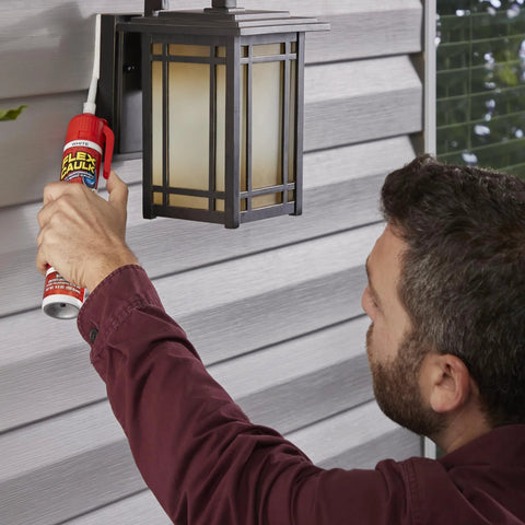 Amazon Flex Caulk 9 oz white sealant being applied to exterior siding near an outdoor lantern