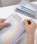 Hands sealing a Glitter Bubble Mailers 30 Pack Tear Resistant Shipping Bags For Jewelry Makeup Gifts And Small Items Thick Protective Mailers.
