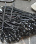Top Shelf 8 Inch Push Mount Nylon Cable Ties With Slick Fir Tree Tips For Indoor And Outdoor Wiring UV Resistant Black Fasteners stacked on a workbench.