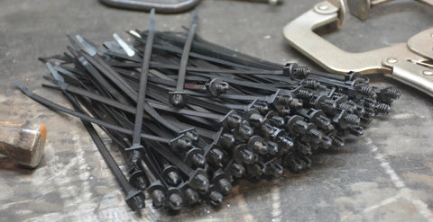 Top Shelf 8 Inch Push Mount Nylon Cable Ties With Slick Fir Tree Tips For Indoor And Outdoor Wiring UV Resistant Black Fasteners stacked on a workbench.