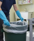Person placing Heavy Duty 40 45 Gallon Trash Bags With Clear Scent Free Build Featuring No Nonsense Tear Resistant Polyethylene And Star Seal Bottom For Straight Up Leak Proof Cleanup In Every Standard Waste Bin into green trash can.
