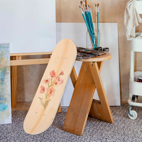 Blank Unfinished 7 Ply Wooden Skateboard Deck With Double Tail For Art Painting And Do It Yourself DIY Custom Builds Replacement Deck featuring floral art leaning against a wooden stool in an art studio.