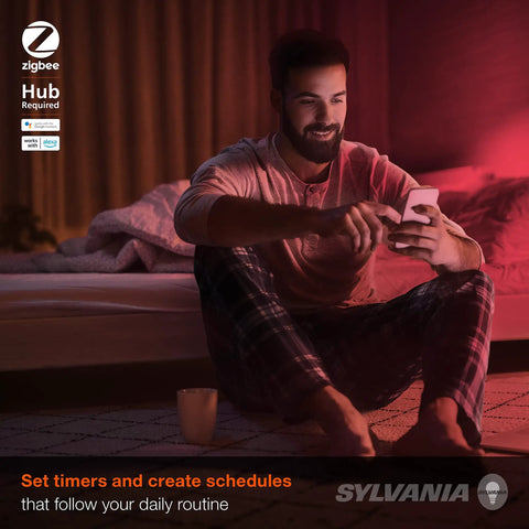 Man in pajamas using smartphone with Smart Color Changing A19 LED Bulb, creating scenes via ZigBee-enabled smart home system