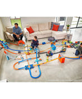 Children playing with Deluxe Stunt Box Track Builder Playset with 25 parts and a 1 to 64 scale vehicle in a living room.