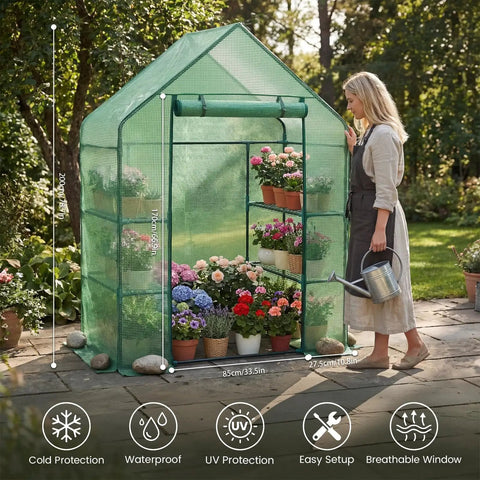 A woman waters plants inside an Outdoor Walk In Greenhouse 55 By 28 By 78 Inches With Three Tier Shelves Tool Free Setup Heavy Duty Durable PE Cover Weather Shield UV Protected For Garden And Backyard on a patio.