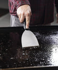 Griddle Cleaning Kit 8 Piece Set For Outdoor Griddles Durable Rust Resistant Tools Heat Resistant Scrapers And Sponges In Black Orange Silver Easy Cleanup After Backyard BBQs And Everyday Grilling Sessions stainless steel scraper on a greasy flat-top griddle