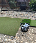 Portable Golf Ball Basket With Handle Holds Up To 50 Balls, Black Ball Bucket on backyard mat with net in view