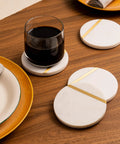 Dope White Marble Coasters Set Of 6 With Gold Brass Inlay For Luxury Aesthetic Modern Coffee Table Decor Real Natural Semi Absorbent Stone Drink Coasters Premium Quality displayed on wooden table with glass and plates.