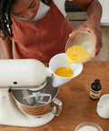 Mess-Free Flour Funnel Attachment for Stand Mixers with Extended Splash Guard being used to pour eggs into mixer bowl.