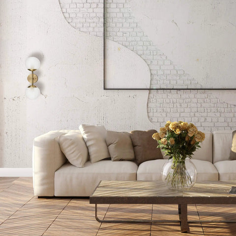 Celestia 2-Light Wall Sconce in matte brass with frosted glass shades in glamorous living room setting with modern decor.
