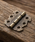 Close-up of a 20 Pack Mini Butterfly Hinges In Vintage Bronze, 90 Degree Folding Hardware With Engraved Pattern on wood surface.