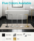 Heavy Duty Freestanding Toilet Paper Holder Stand In Matte Gold Frame standing among black, silver, white, and gold colors in a bathroom.