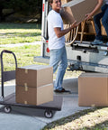Foldable Heavy Duty Push Cart Dolly With 660 Lb Capacity And Swivel Wheels for loading boxes into a truck in a driveway setting.