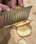 Crinkle-cut blade slicer, stainless steel handheld kitchen tool; close-up of apple slicing on cutting board.