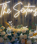 Wedding neon sign 'The Sextons' in warm white LED with floral arrangement and candles