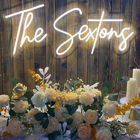 Wedding neon sign 'The Sextons' in warm white LED with floral arrangement and candles