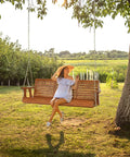 Woman sitting on Built Tough Outdoor Wooden Porch Swing With Adjustable Chains 880 Lb Capacity 5 Ft Brown Garden Bench Seat