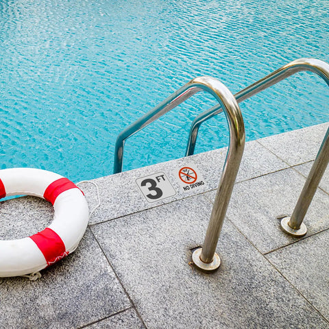 Poolside view with a 3ft depth sticker and no diving sign on the deck near a ladder and lifebuoy.