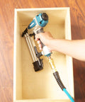 Hand holding Rock Solid 18 Gauge 2 Inch Brad Nailer Kit inside a wood box with an air hose connected for pneumatic operation.