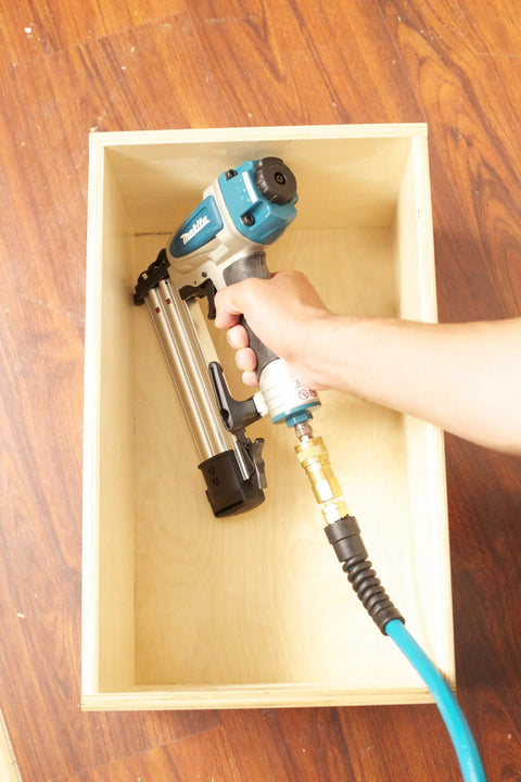 Hand holding Rock Solid 18 Gauge 2 Inch Brad Nailer Kit inside a wood box with an air hose connected for pneumatic operation.