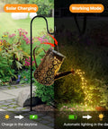 Solar Powered Watering Can Lantern Lights For Garden Decor hanging on hook with LED string lights illuminating pathway
