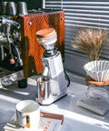 Kickstart Your Daily Grind With This Rock Solid Electric Coffee Grinder Featuring 40Mm Conical Titanium Burrs 19 Straight Forward Settings And A Generous 75G Bean Hopper For Fresh Bold Sips And Zero Hassle Cleanup Guaranteed, placed next to an espresso machine and coffee accessories.