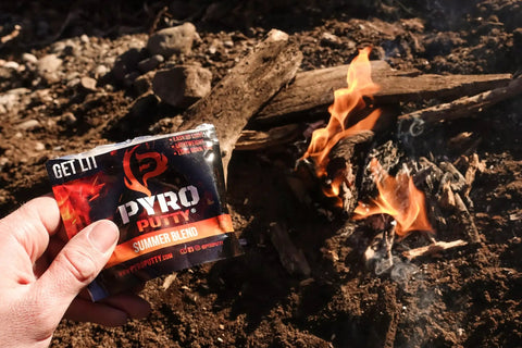 Hand holding Pyro Putty Emergency Fire Starter For All Seasons Eco Blend Waterproof And Windproof 2 Oz Can Ready For Winter Or Summer Use Unlimited Shelf Life Survival Tool For Camping Hiking And Emergencies near a fire.