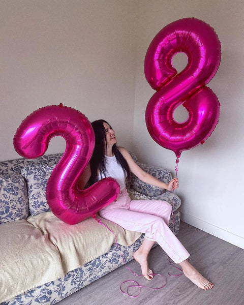 Woman holding hot pink number 2 and number 8 balloons on a couch, featuring Hot Pink Number 8 Balloon 40 Inch Giant Foil Balloon for Party Supplies.