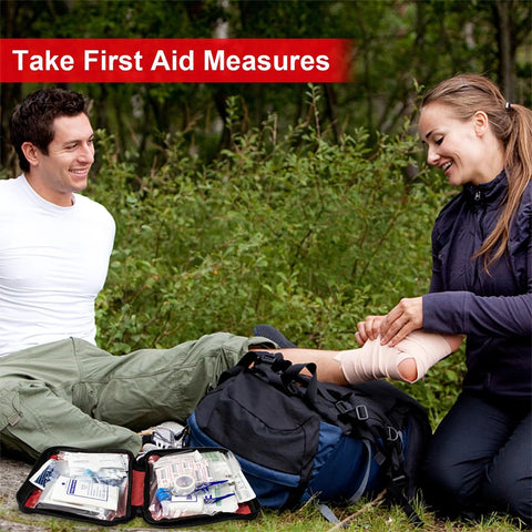 Front view of portable red travel first aid kit opened outdoors beside a backpack with medical supplies.
