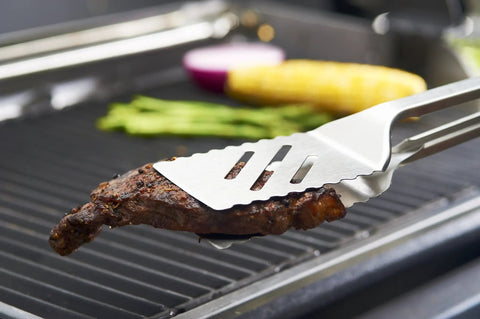 16-Inch Stainless Steel Tong And Turner Combo With Red Soft Grip Inserts holding steak on grill