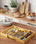 Expandable Bamboo Silverware Organizer For Drawers, Ultra Roomy 6 To 8 Slot Utensil Tray on kitchen counter with utensils
