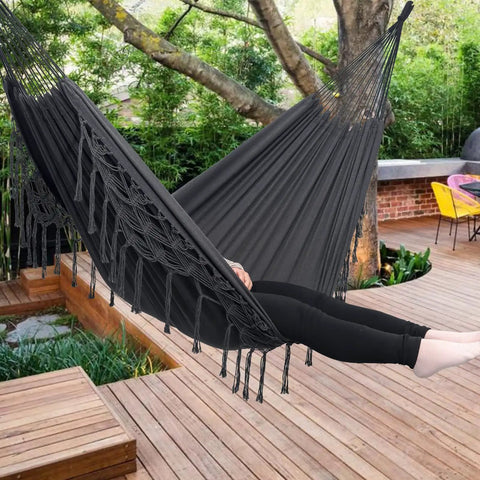 Boho Macrame Hammock With Elegant Tassels For Patio And Yard Cozy And Chill For Indoor Or Outdoor Use 450 Pound Capacity Includes Tie Ropes And Drawstring Bag Dark Grey hanging on wooden deck