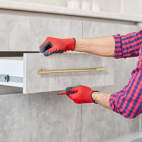 Person installing No Nonsense Solid Brass Cabinet Pulls With Sleek Brushed Gold Finish on a gray drawer front.