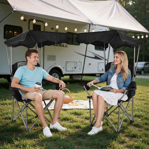 Two people sitting on Folding Camping Chair With Canopy Shade And Cup Holders, relaxing near RV with picnic setup.