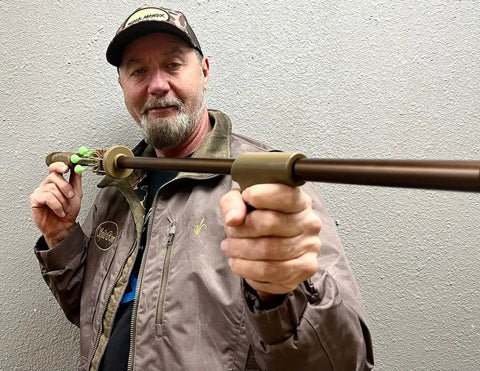Person holding Slock Master Blow Gun 5 Foot Long 625 Big Bore Caliber with Pistol Grip, Dart Quiver, and Anodized Bronze Finish.