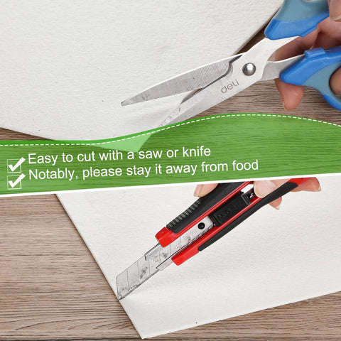 White ceramic fiber kiln paper sheet being cut with blue-handled scissors on wood.
