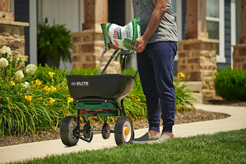 Person pouring All Grass Types Lawn Fertilizer Twin Pack For 5000 Sq Ft Coverage 12.5 Lb into a spreader on lawn