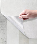 Hand holding Knockout Look Waterproof Peel And Stick Wallpaper Roll featuring textured finish against concrete backdrop.