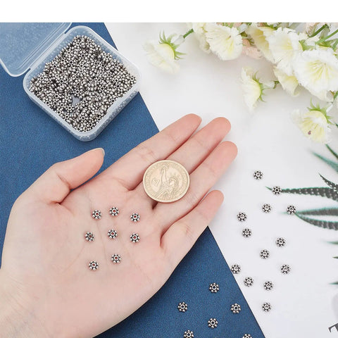 Hand holding Antique Silver Daisy Flower Spacer Beads 6mm 300Pcs, showing size comparison with a coin, for Tibetan style jewelry making.