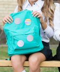 Backpack with 160 Pcs Colorful Holographic Badge Film For Button Makers 58mm Two And A Quarter Inch attached, showing glittery styles.