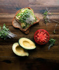 Avocado toast with colorful microgreen seeds mix, sliced tomato, and avocado on a wooden table.
