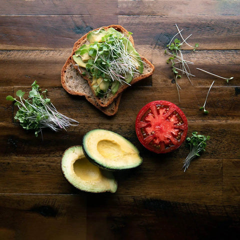 Avocado toast with colorful microgreen seeds mix, sliced tomato, and avocado on a wooden table.