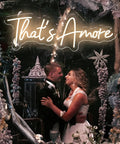 Couple under 'That's Amore' LED neon sign in wedding decor with flowers and lights.