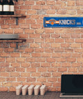 New York Knicks Metal Street Wall Sign Four By Fifteen Inches Heavy Duty Aluminum Game Day Home Office Man Cave Decor mounted on brick wall.