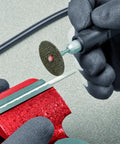 Hands operating a metal tool on a red heavy duty base with a rotating disk for Shop Ready Double Wheel Bench Grinder With Adjustable Spark Arresters And Heavy Duty Tool Rests Featuring Full Safety Shrouds Plus Four Rugged Grip Rubber Mounts For Serious Grinding And Polishing Jobs.