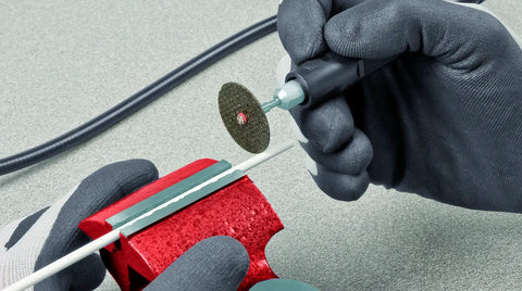Hands operating a metal tool on a red heavy duty base with a rotating disk for Shop Ready Double Wheel Bench Grinder With Adjustable Spark Arresters And Heavy Duty Tool Rests Featuring Full Safety Shrouds Plus Four Rugged Grip Rubber Mounts For Serious Grinding And Polishing Jobs.