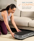 Woman storing Waver Vibration Plate Exercise Machine with High Intensity Full Body Vibration under a sofa.