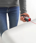 Hand holding Laser Distance Meter TC LD 25, measuring 0.05 to 25 meters with visible red laser beam, ideal for precise measurements.